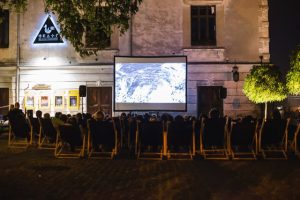 Zdjęcie ekranu kinowego i siedzącej przed nim publiczności w plenerze podczas wydarzenia kulturalnego.
