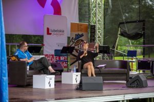 Zdjęcie siedzących na scenie mężczyzny oraz kobiety przemawiającej do mikrofonu.